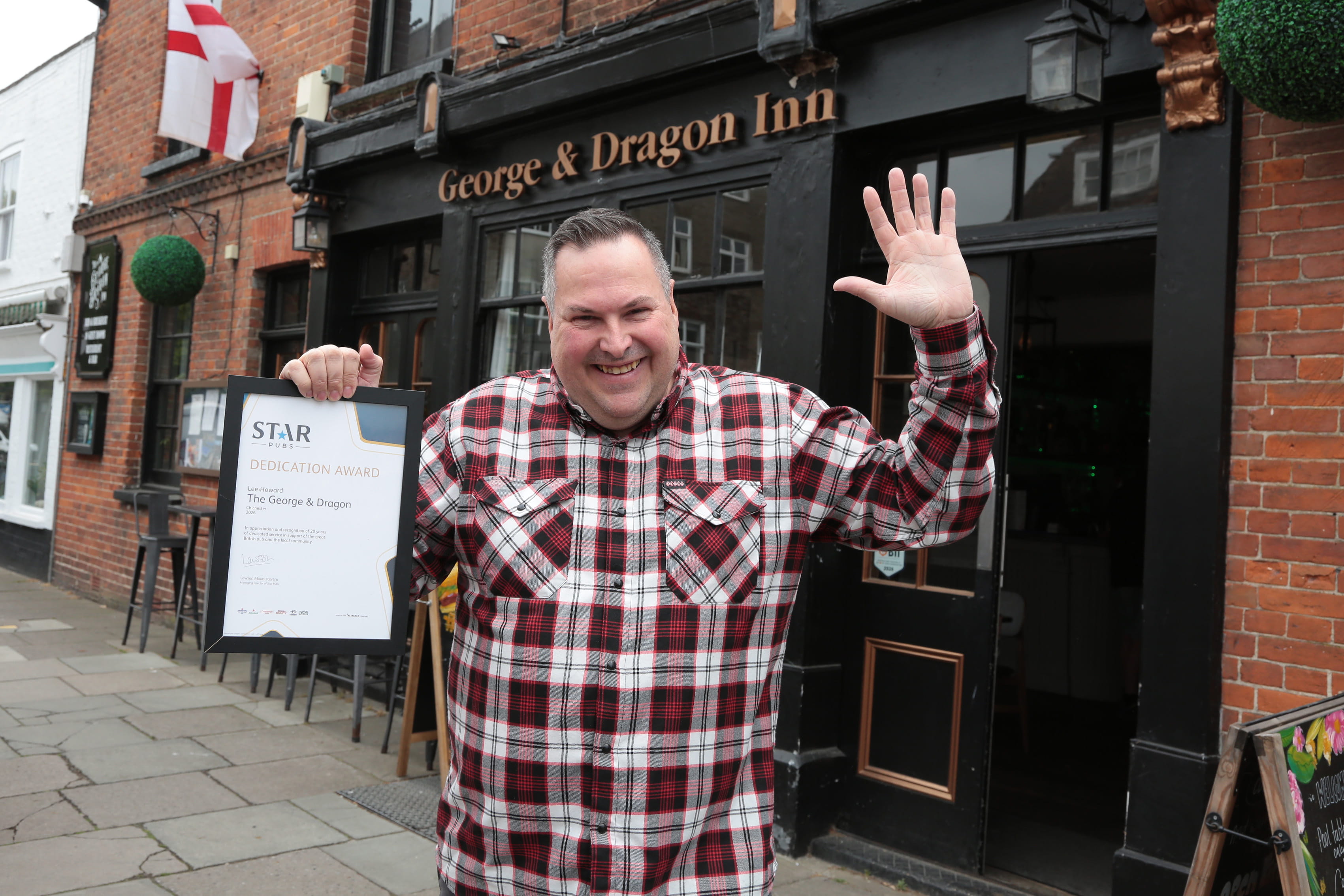 Male pub licensee stood outside of his pub with a certificate