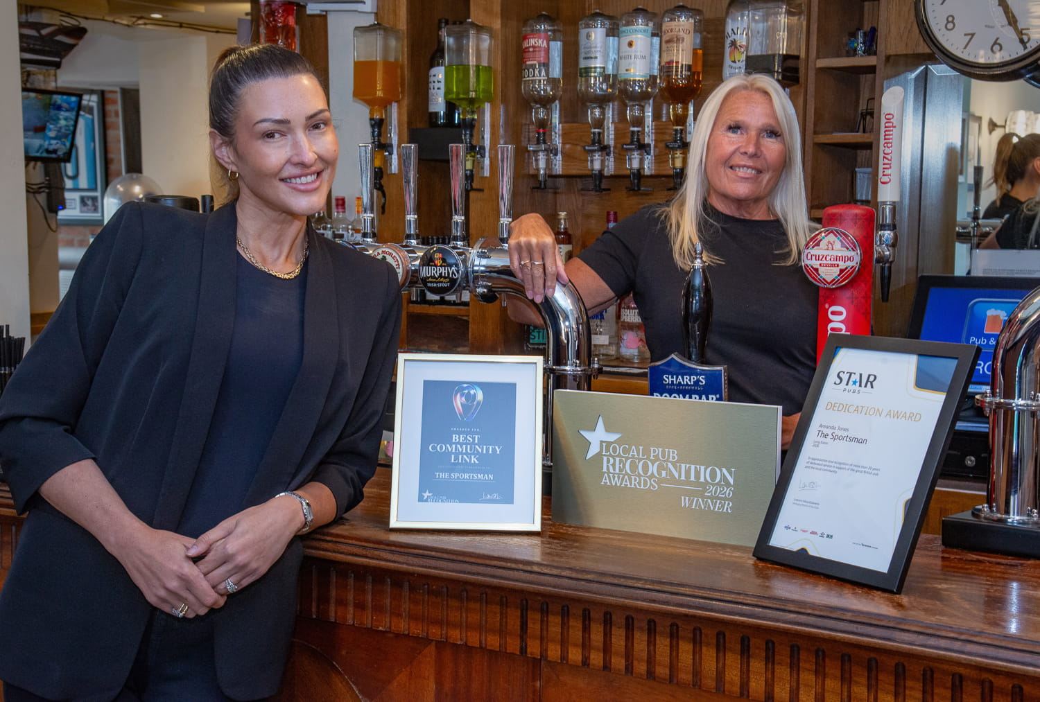 A female pub licensee standing behind the bar with three awards sitting on the bar top