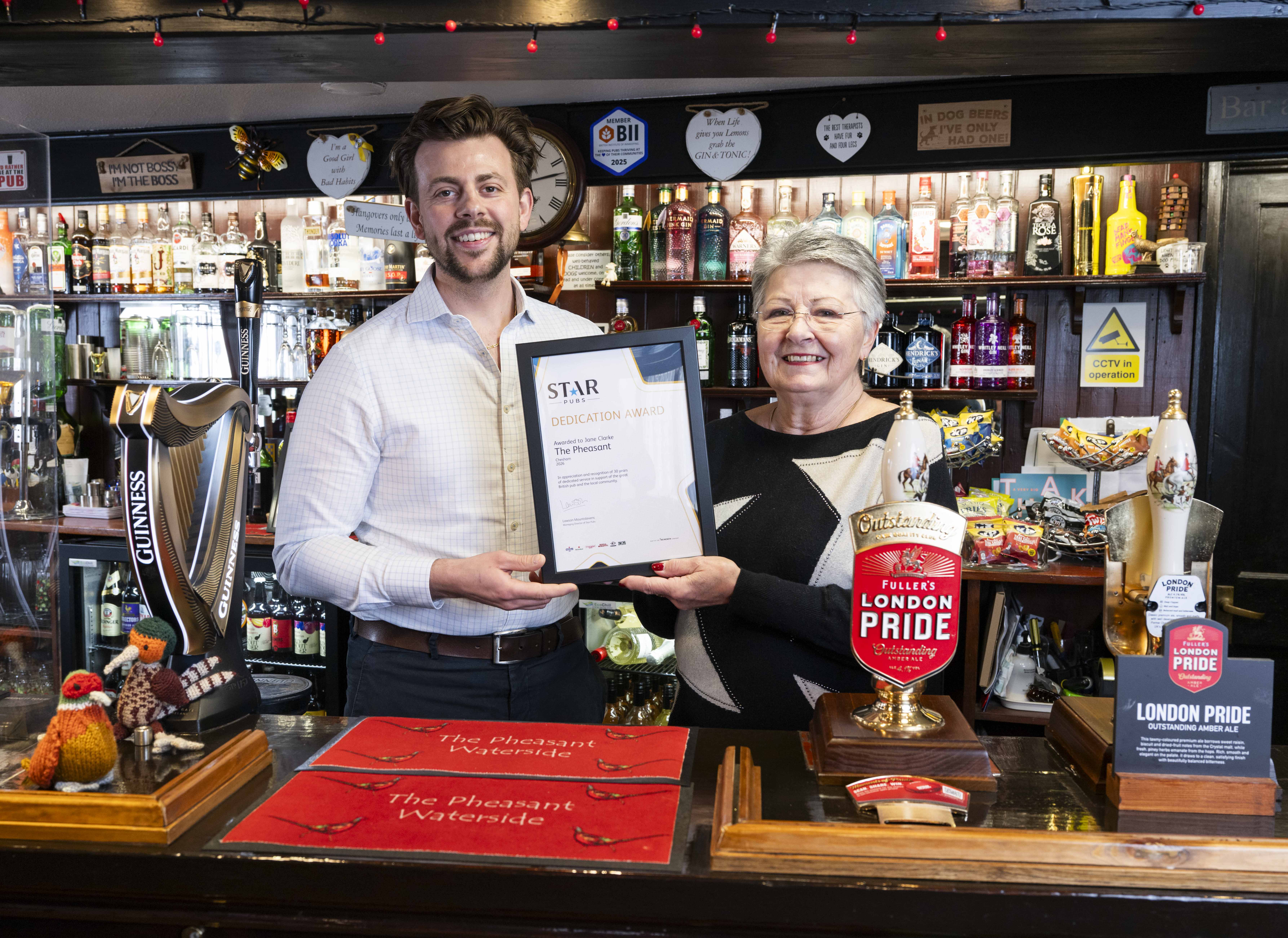 Female pub licensee and her male business development manager standing behind the bar holding an award
