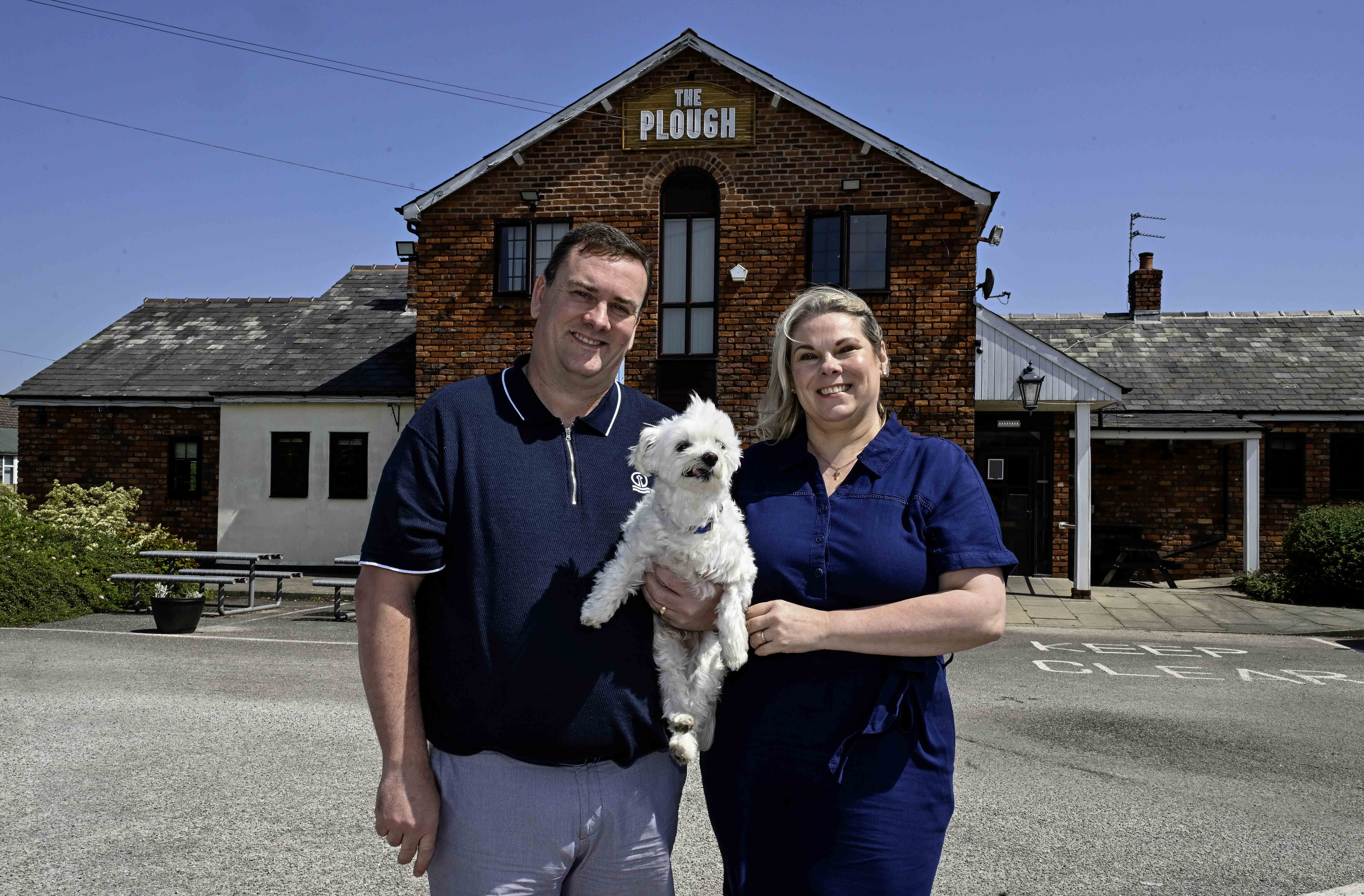 Man and woman standing outside a pub holding a small white dog