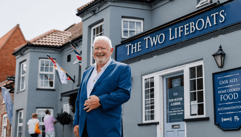 The Two Lifeboats' owner standing in front of his pub smiling