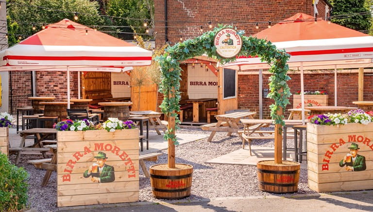 A pub garden decorated with plants and Birra Moretti signs