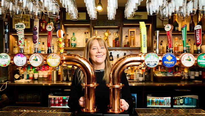 Woman standing behind the taps at her pub
